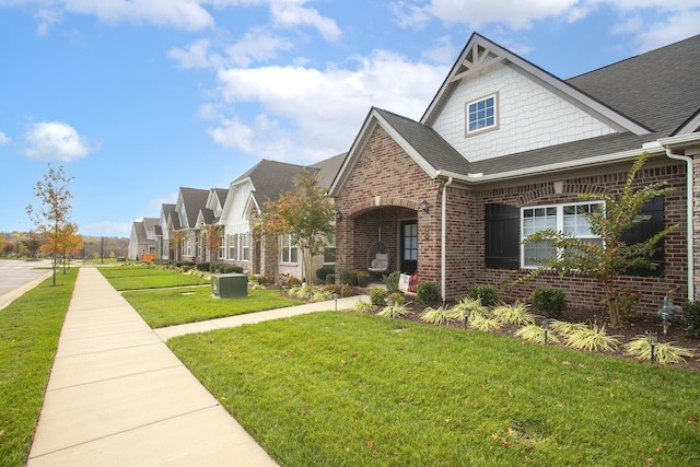view of front of house featuring roof with shingles, a residential view, brick siding, central AC, and a front lawn
