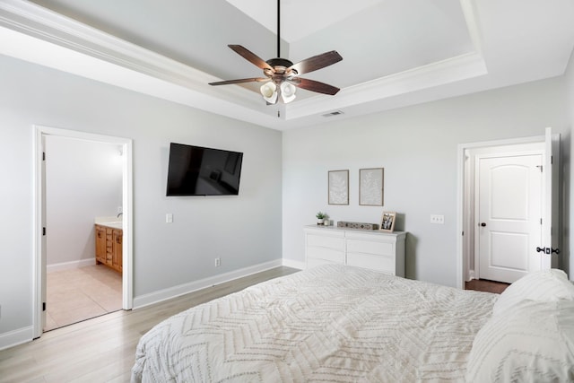 bedroom with light wood-style floors, ornamental molding, connected bathroom, and a tray ceiling
