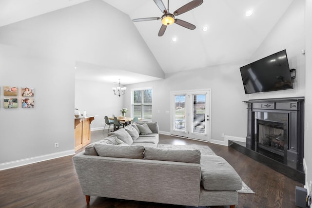 living room featuring wood finished floors, baseboards, high vaulted ceiling, a fireplace with raised hearth, and ceiling fan with notable chandelier