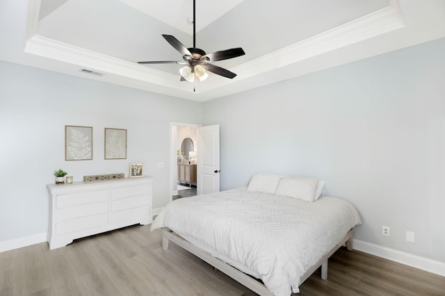 bedroom featuring visible vents, ornamental molding, wood finished floors, baseboards, and a raised ceiling
