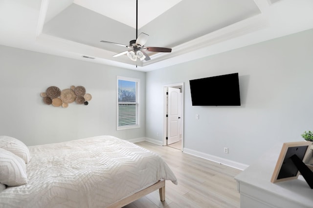 bedroom featuring baseboards, a tray ceiling, light wood-style flooring, and visible vents