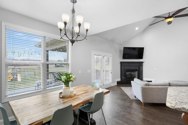 dining space with a fireplace with raised hearth, ceiling fan with notable chandelier, baseboards, vaulted ceiling, and dark wood-style floors