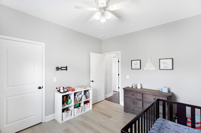 bedroom featuring baseboards, light wood finished floors, ceiling fan, and a crib