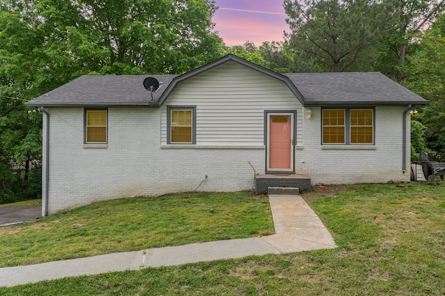 view of front of home featuring brick siding, roof with shingles, and a front yard
