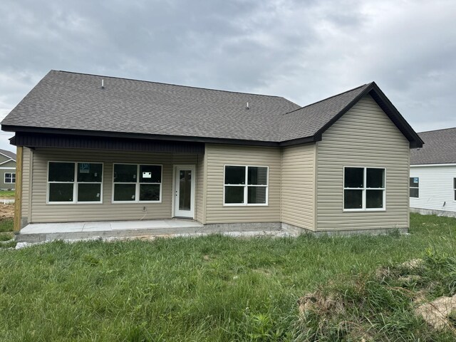back of property with a yard, a shingled roof, and a patio area