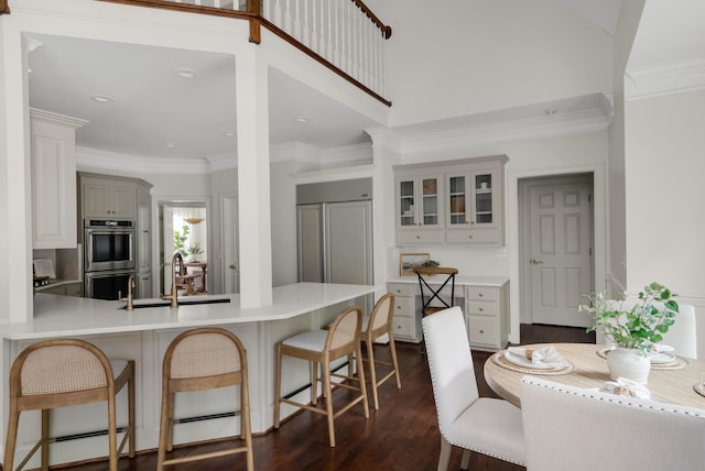 kitchen featuring a kitchen bar, a sink, double oven, a peninsula, and glass insert cabinets