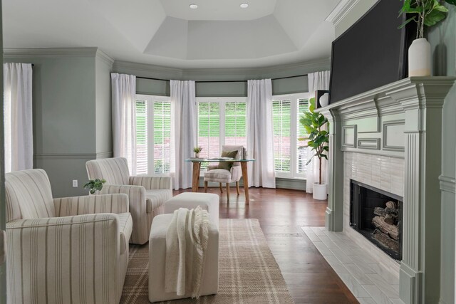interior space with wood finished floors, a wealth of natural light, a raised ceiling, and a tile fireplace