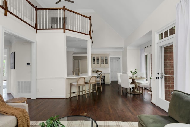 living room with ceiling fan, visible vents, crown molding, dark wood finished floors, and high vaulted ceiling