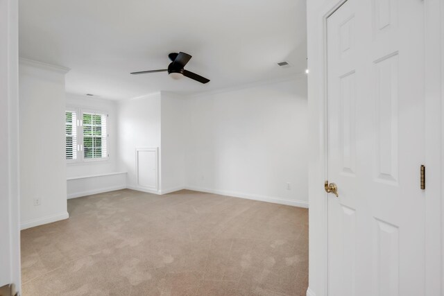 spare room featuring a ceiling fan, visible vents, crown molding, baseboards, and light carpet