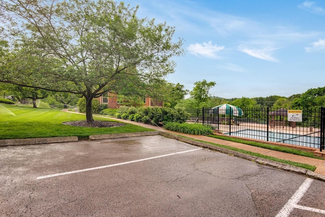uncovered parking lot featuring a community pool and fence