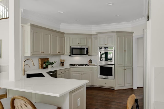 kitchen featuring a kitchen bar, appliances with stainless steel finishes, a sink, light countertops, and a peninsula