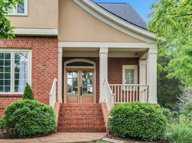 view of exterior entry with a shingled roof, stucco siding, and brick siding