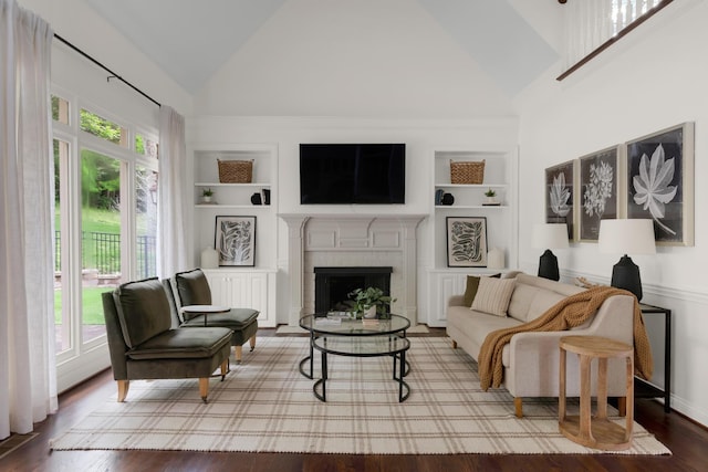 living area with built in features, wood finished floors, a fireplace, baseboards, and high vaulted ceiling