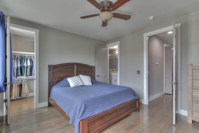 bedroom with a walk in closet, baseboards, a closet, and wood finished floors
