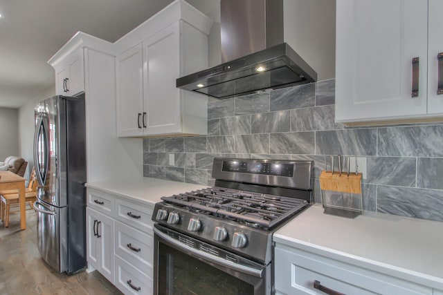 kitchen featuring wall chimney range hood, decorative backsplash, light countertops, stainless steel appliances, and white cabinetry
