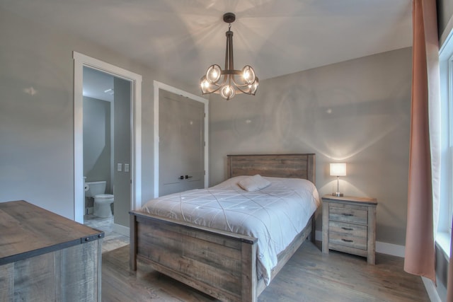 bedroom with ensuite bathroom, baseboards, wood finished floors, and a notable chandelier