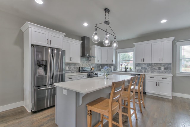 kitchen with wall chimney range hood, a center island, tasteful backsplash, stainless steel appliances, and white cabinetry