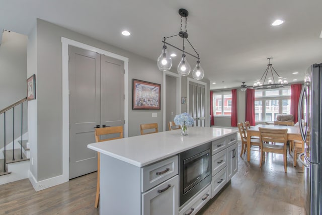 kitchen featuring freestanding refrigerator, wood finished floors, a center island, light countertops, and built in microwave