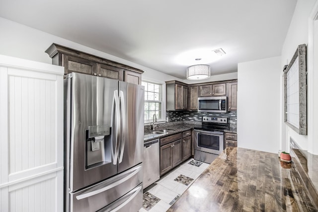 907 N Graycroft Ave, Madison, TN 37115 - kitchen with stainless steel appliances, dark brown cabinets, a sink, decorative backsplash, and dark stone counters