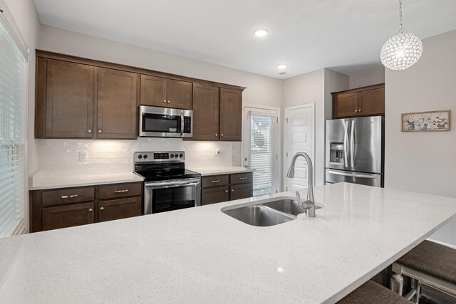 kitchen with a kitchen bar, a sink, backsplash, hanging light fixtures, and stainless steel appliances