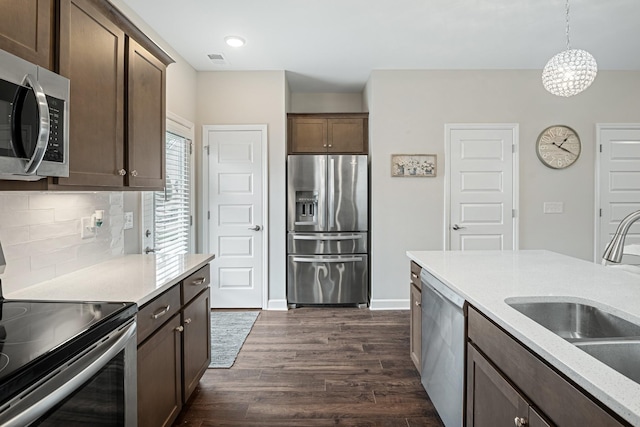 kitchen featuring dark brown cabinets, a sink, stainless steel appliances, decorative backsplash, and dark wood-type flooring