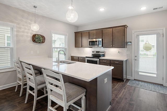 kitchen featuring appliances with stainless steel finishes, a sink, a kitchen breakfast bar, dark wood finished floors, and baseboards