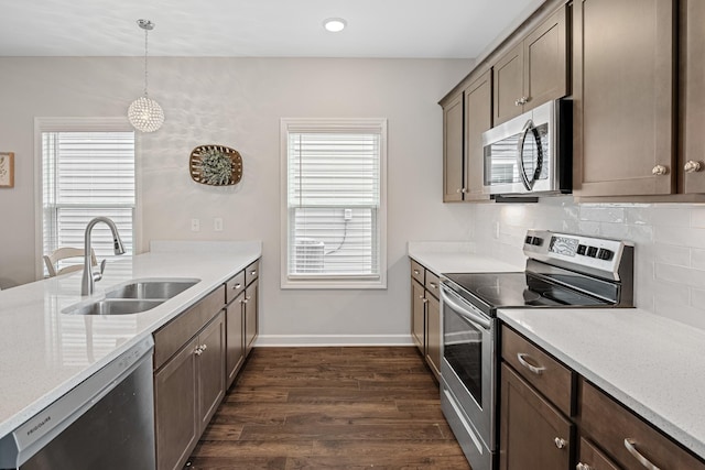 kitchen featuring backsplash, appliances with stainless steel finishes, a sink, baseboards, and dark wood-type flooring