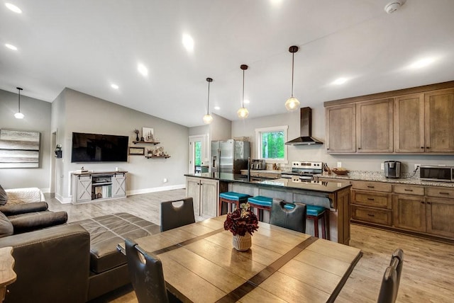 kitchen featuring open floor plan, light wood-style flooring, wall chimney range hood, and stainless steel appliances
