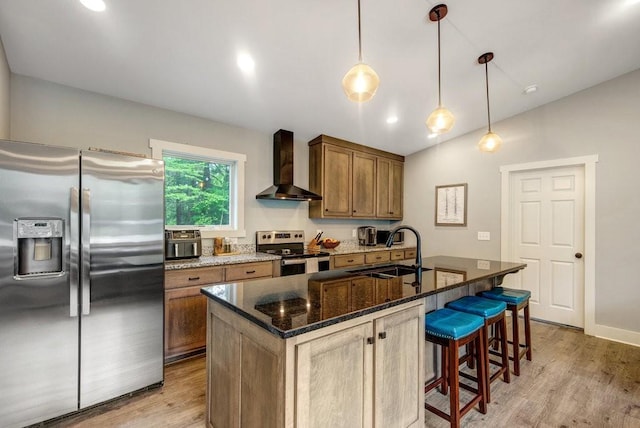 kitchen featuring a sink, wall chimney exhaust hood, dark stone counters, stainless steel appliances, and light wood-type flooring