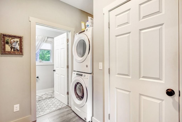 clothes washing area with baseboards, stacked washer and clothes dryer, light wood-style flooring, and laundry area