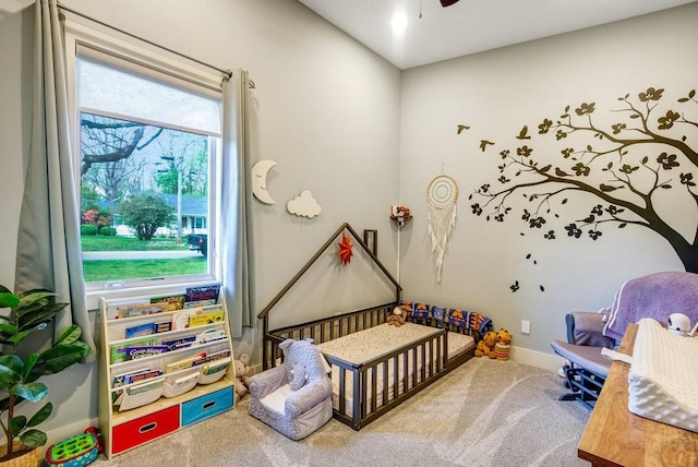 bedroom featuring a nursery area, ceiling fan, baseboards, and carpet flooring