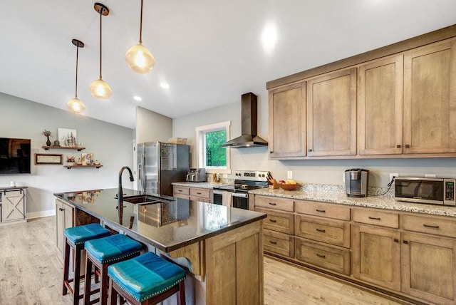kitchen with a sink, light wood-style flooring, stainless steel appliances, and wall chimney exhaust hood