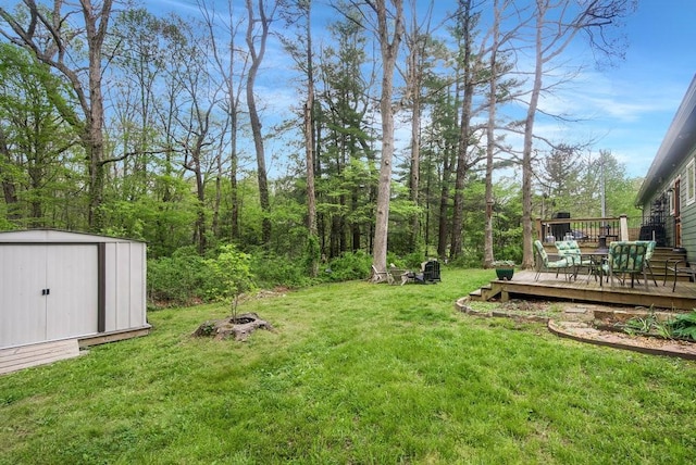 view of yard featuring a storage shed, a wooden deck, an outdoor structure, and a fire pit