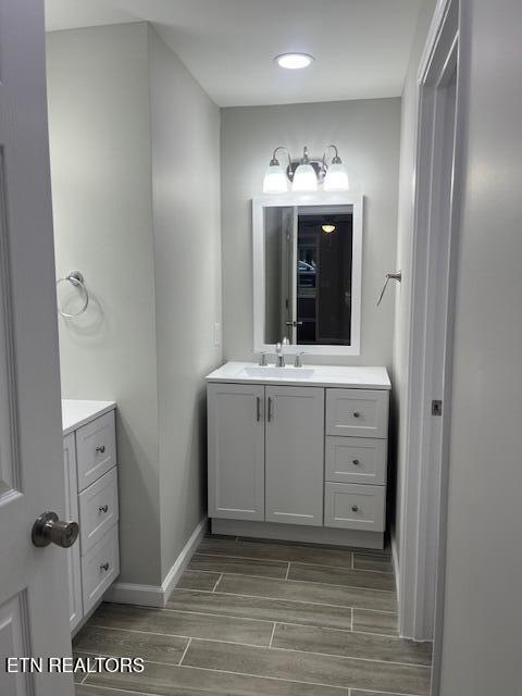 bathroom featuring baseboards, vanity, wood finish floors, and recessed lighting
