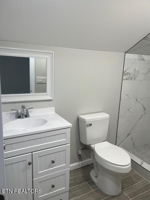 full bath with toilet, marble finish floor, baseboards, a tile shower, and vanity