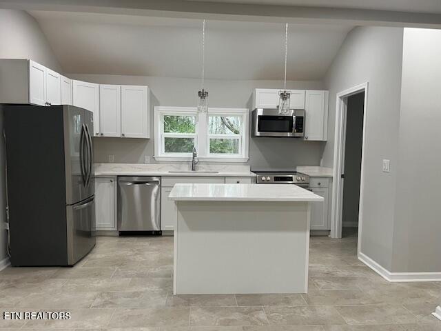 kitchen featuring a sink, stainless steel appliances, vaulted ceiling, light countertops, and a center island