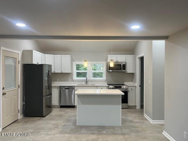 kitchen featuring a sink, stainless steel appliances, vaulted ceiling, light countertops, and a kitchen island