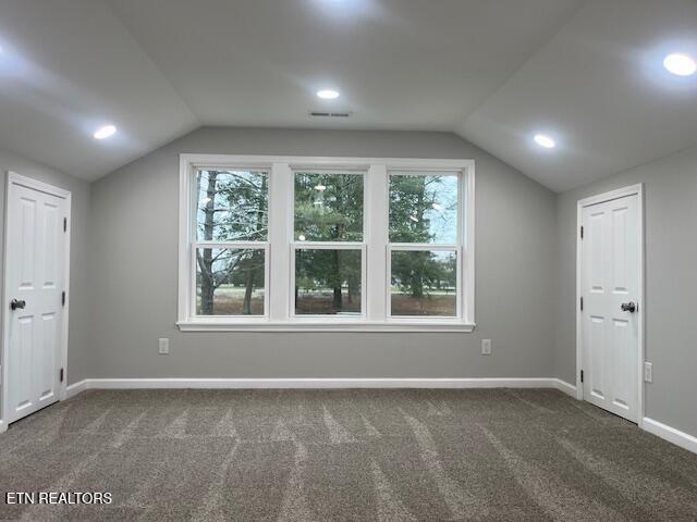 additional living space featuring vaulted ceiling, dark colored carpet, and baseboards