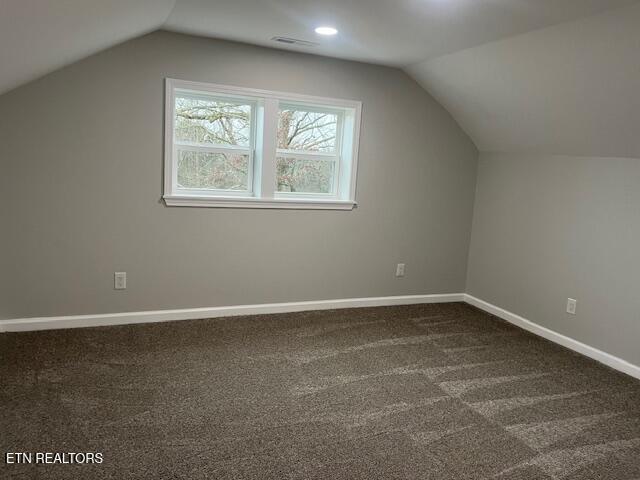 additional living space with lofted ceiling, baseboards, visible vents, and dark carpet