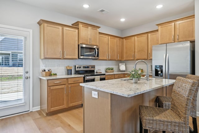 kitchen with visible vents, appliances with stainless steel finishes, a sink, light stone counters, and light wood-style floors