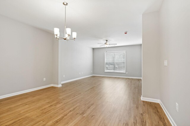 empty room with baseboards, ceiling fan with notable chandelier, and light wood-style floors