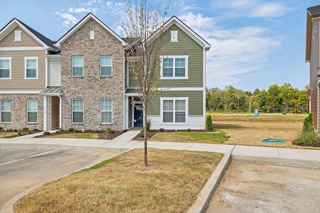view of property with brick siding, uncovered parking, and a front lawn