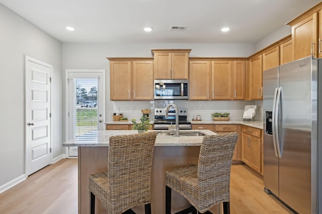 kitchen with light wood-type flooring, a sink, appliances with stainless steel finishes, and backsplash