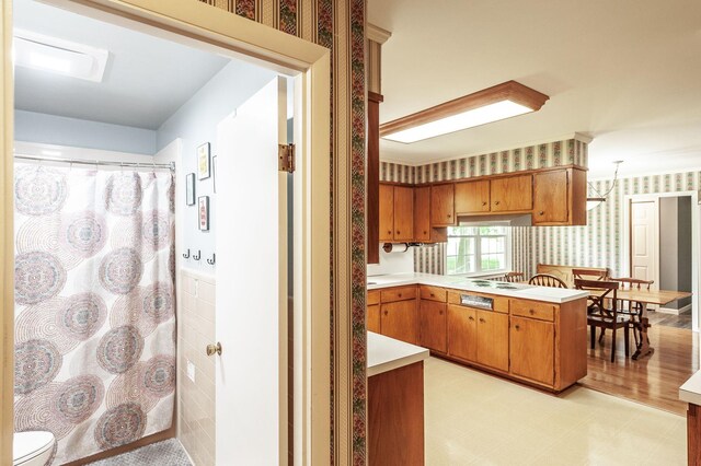 kitchen with brown cabinets, light countertops, a peninsula, light floors, and wallpapered walls