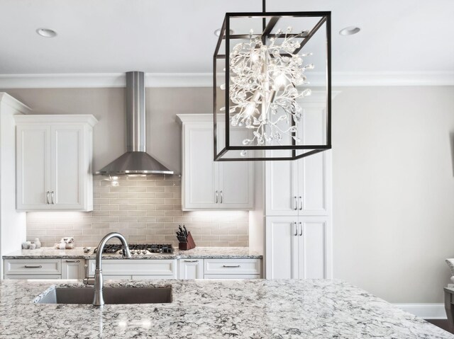 kitchen featuring crown molding, wall chimney exhaust hood, white cabinetry, tasteful backsplash, and a sink