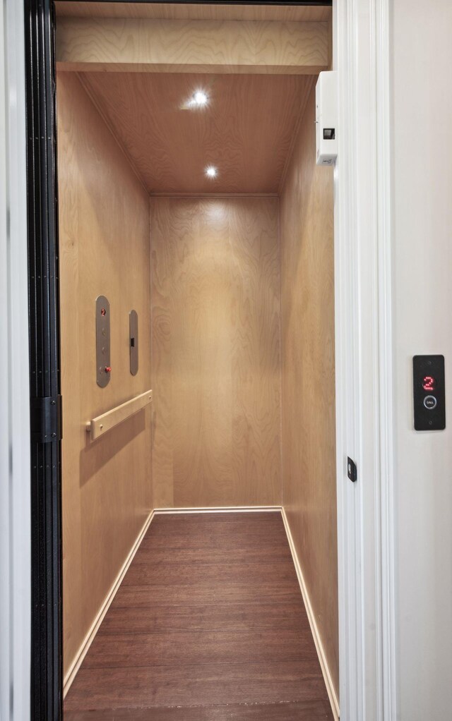 interior details featuring recessed lighting, wooden walls, wood finished floors, and elevator