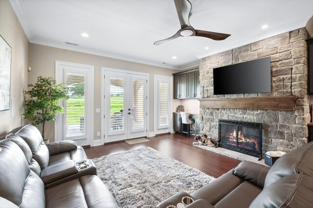 living room with ceiling fan, a stone fireplace, recessed lighting, dark wood-type flooring, and ornamental molding