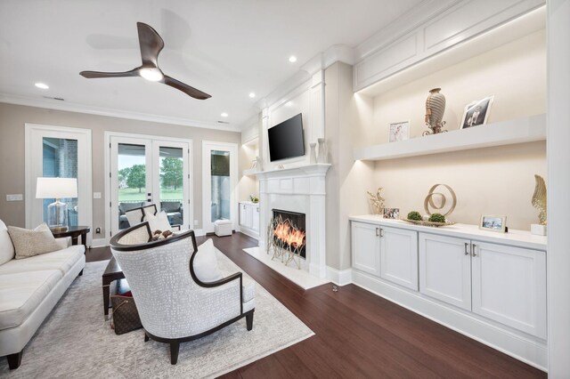 living room featuring crown molding, a lit fireplace, dark wood-type flooring, recessed lighting, and a ceiling fan