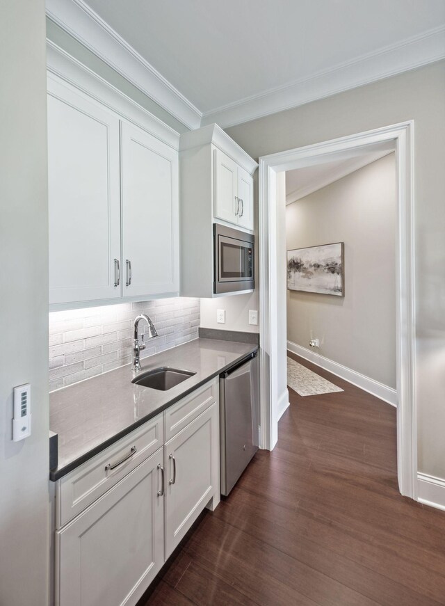 kitchen with backsplash, a sink, ornamental molding, stainless steel appliances, and white cabinetry
