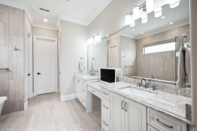 full bath featuring crown molding, a tile shower, a sink, two vanities, and visible vents